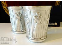 Two pewter cups with female dancers from different cultures.