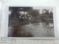 An old photo of young people sitting on the bank in front of the bridge