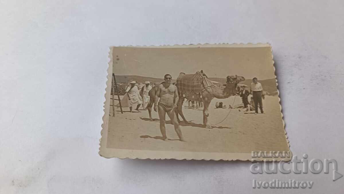 Φωτογραφία Νέου Άνδρα μπροστά σε καμήλα στην παραλία