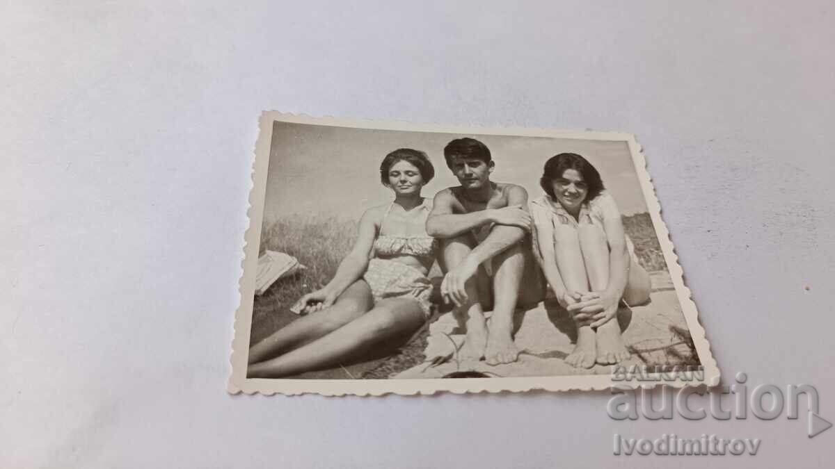 Fotografie: Tânăr și două fete șezând pe iarbă