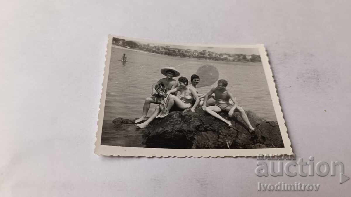 Photo of Young Men and Women Sitting on a Cliff Overlooking the Sea