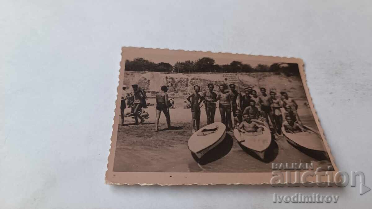 Fotografie cu bărbați și tineri lângă canoe pe malul mării