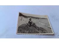 Photo of a young woman sitting on a rock by the sea