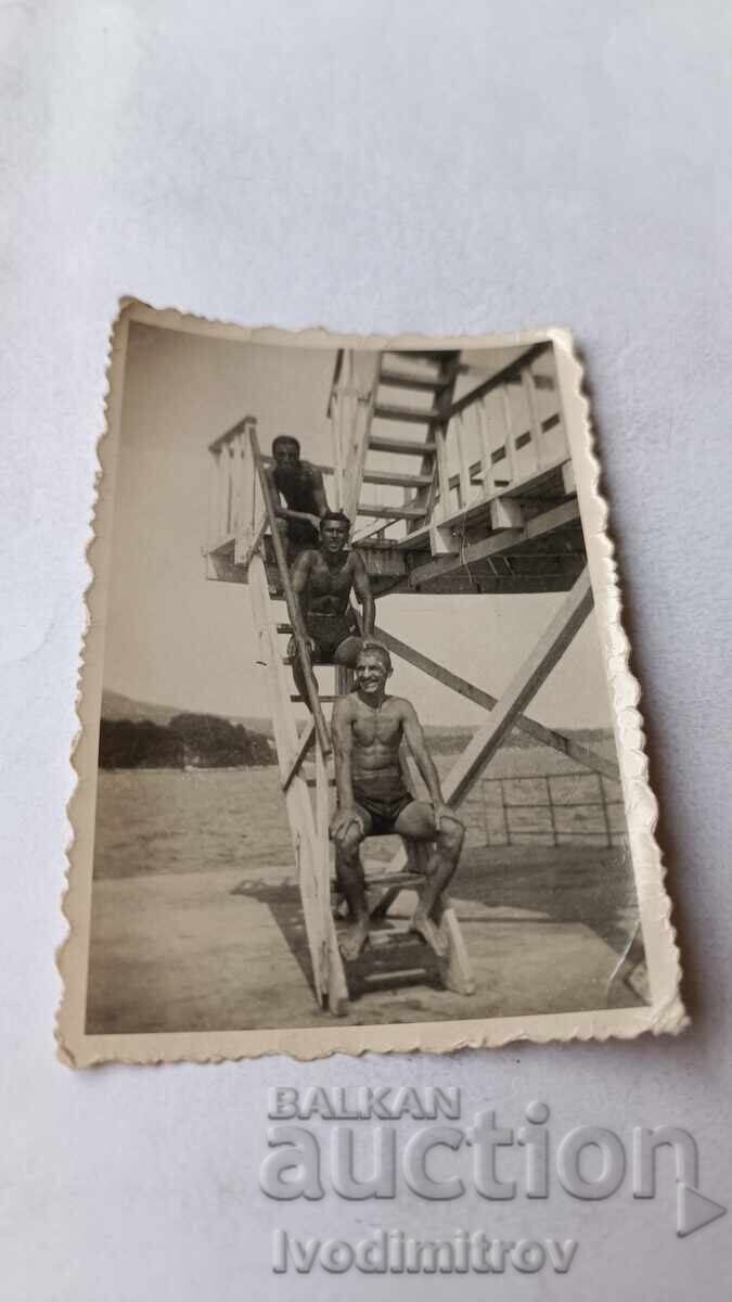 Photo of three young men sitting on the stairs of a pier