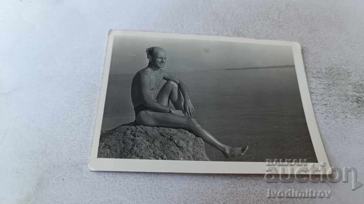 Φωτογραφία Άνδρας που κάθεται σε βράχο πάνω από τη θάλασσα