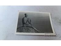 Photo of a man sitting on a cliff overlooking the sea