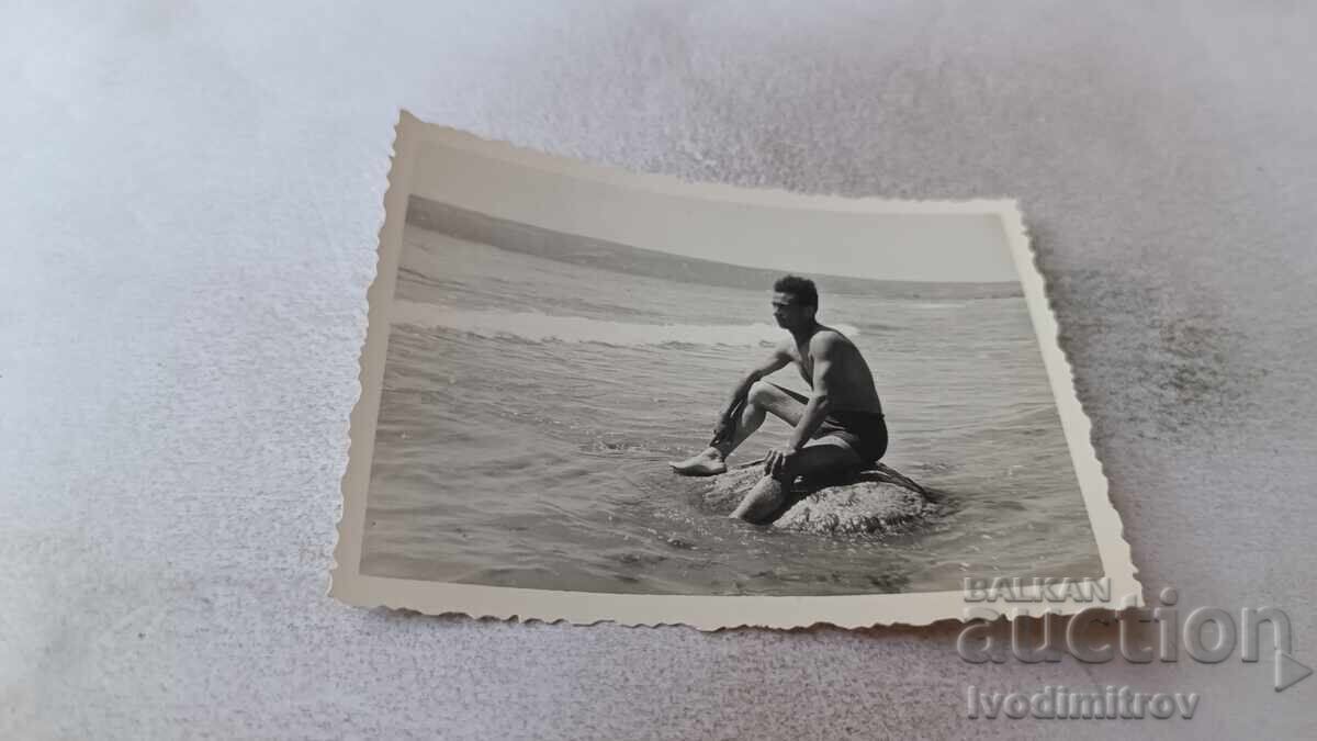 Φωτογραφία Νέος άνδρας κάθεται σε βράχο στη θάλασσα