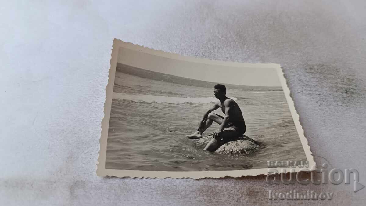 Photo: Young man sitting on a rock in the sea
