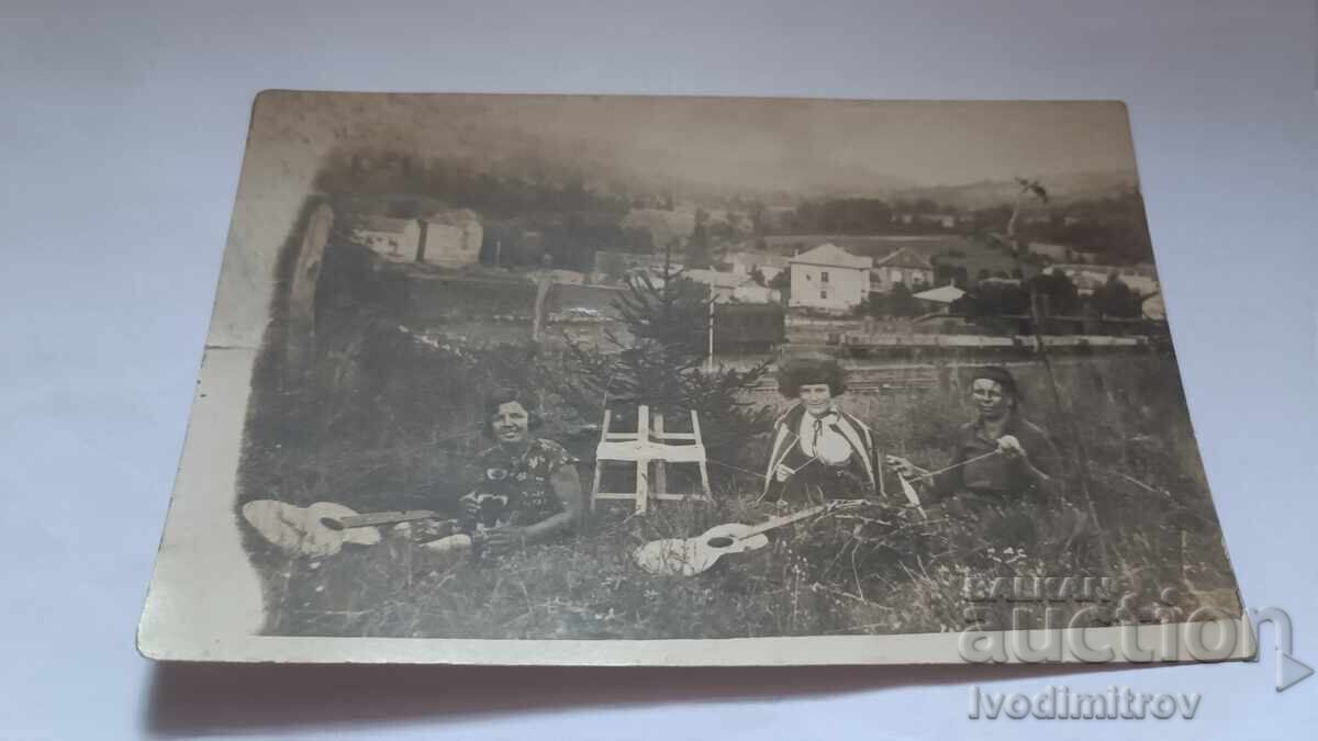 Φωτογραφία Νέων κοριτσιών με κιθάρες και γυναίκας με αδράχτι στο γρασίδι