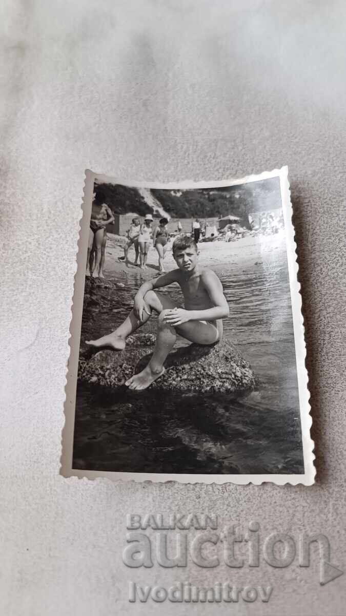 Φωτογραφία Νέου που κάθεται σε βράχο στην παραλία