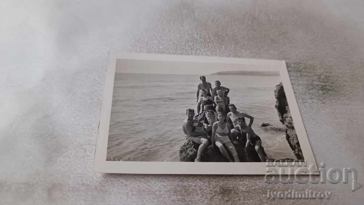 Photo of men, women, and children on a rock on the seashore Photo of men, women, and children on a rock on the seashore
