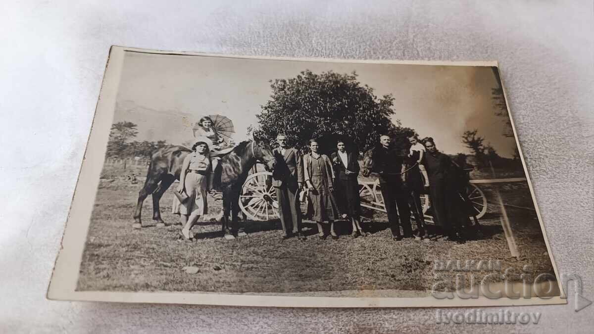 Photo of young girls, men, and a baby with two black horses