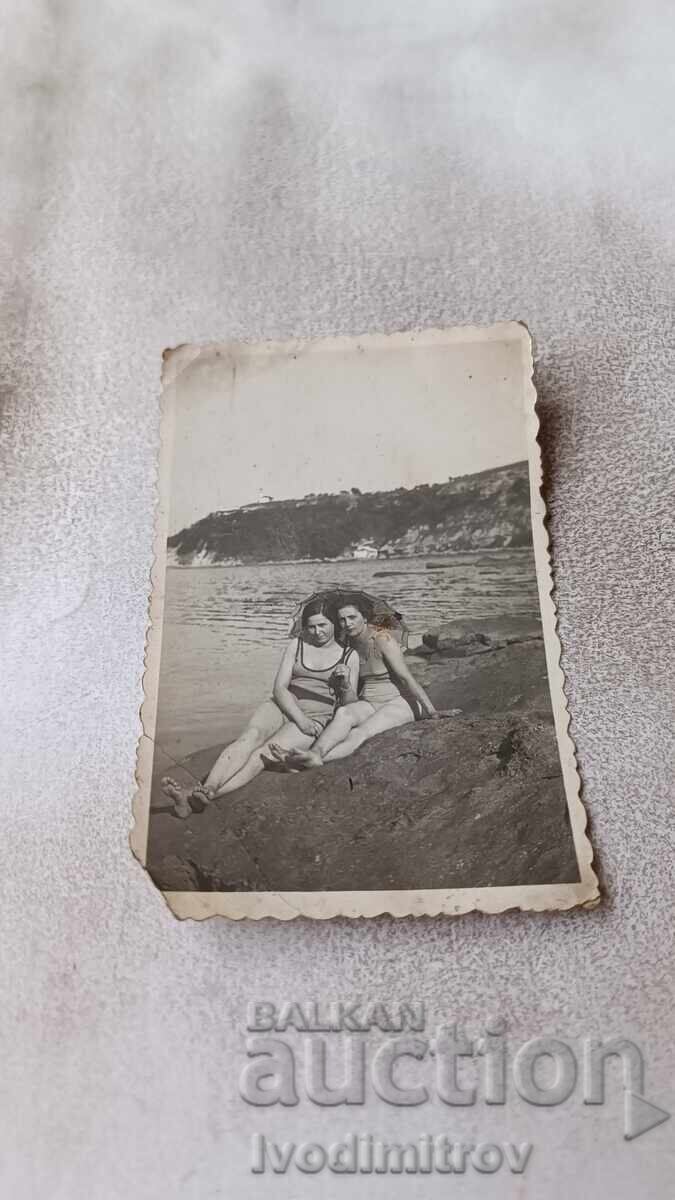 Fotografie Două fete tinere cu umbrelă pe o stâncă deasupra mării