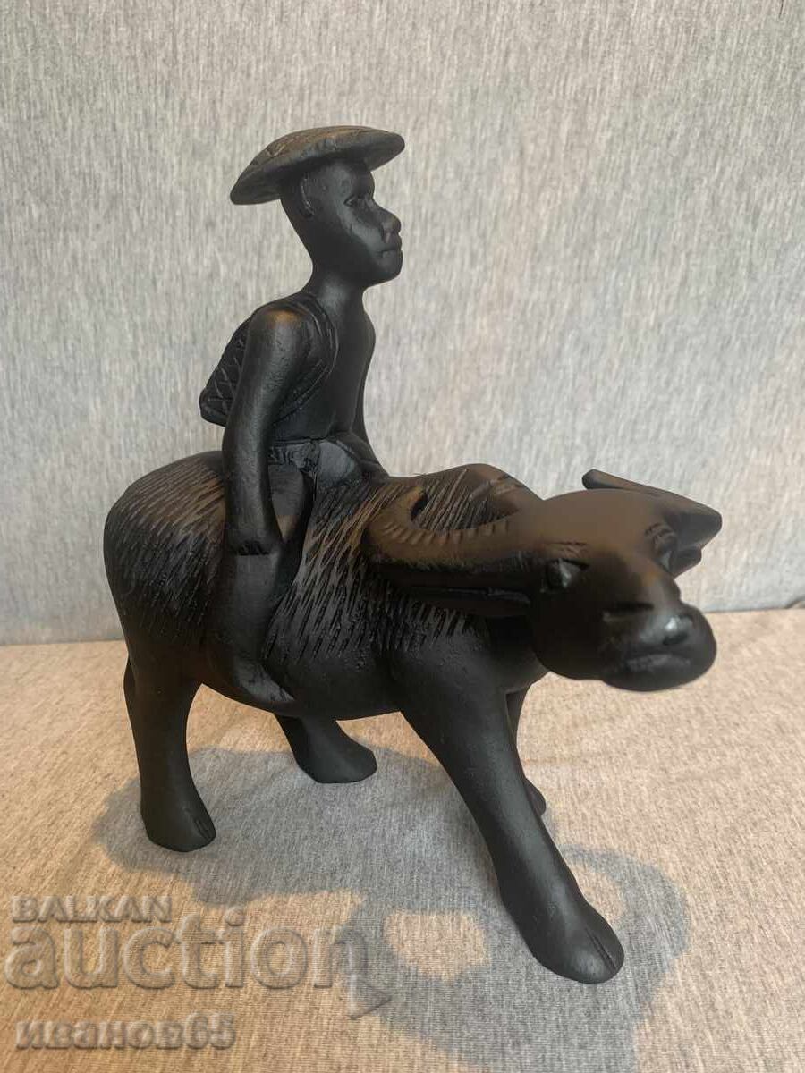 дървена фигурка на азиатски мъж, яздещ бивол