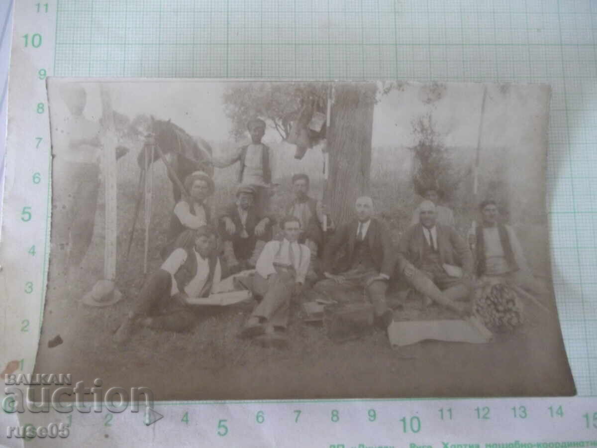 Fotografie cu un grup de bărbați la picnic așezați sub un copac vechi
