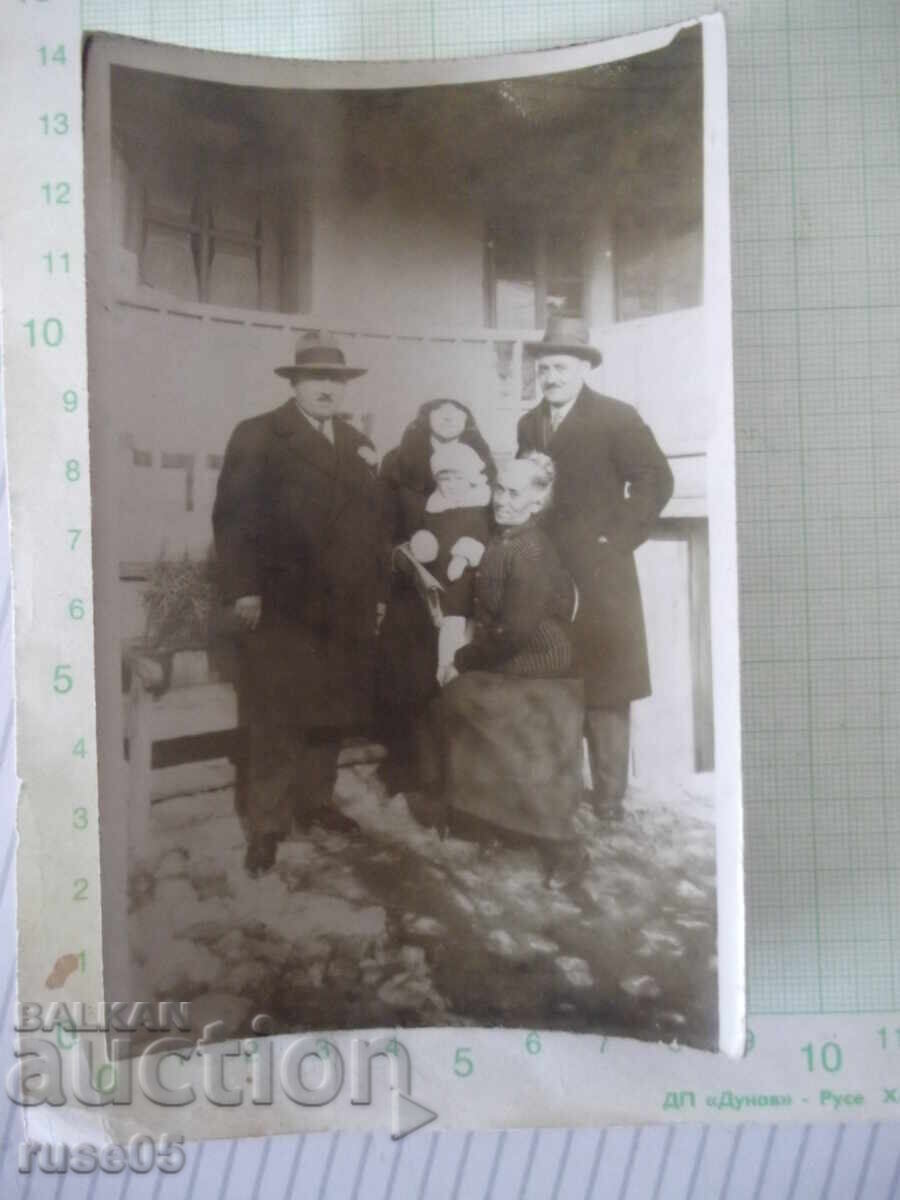 Fotografie cu doi bărbați și două femei cu un copil în fața unei case vechi