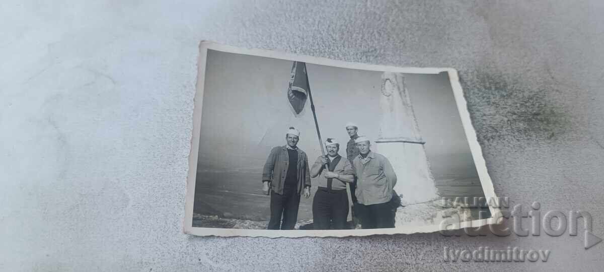 Fotografie Patru bărbați cu un steag în fața unui monument militar