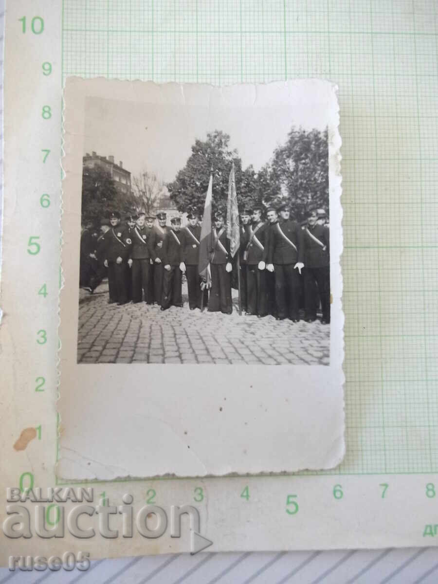 Old photo of uniformed men with two flags on cobblestones