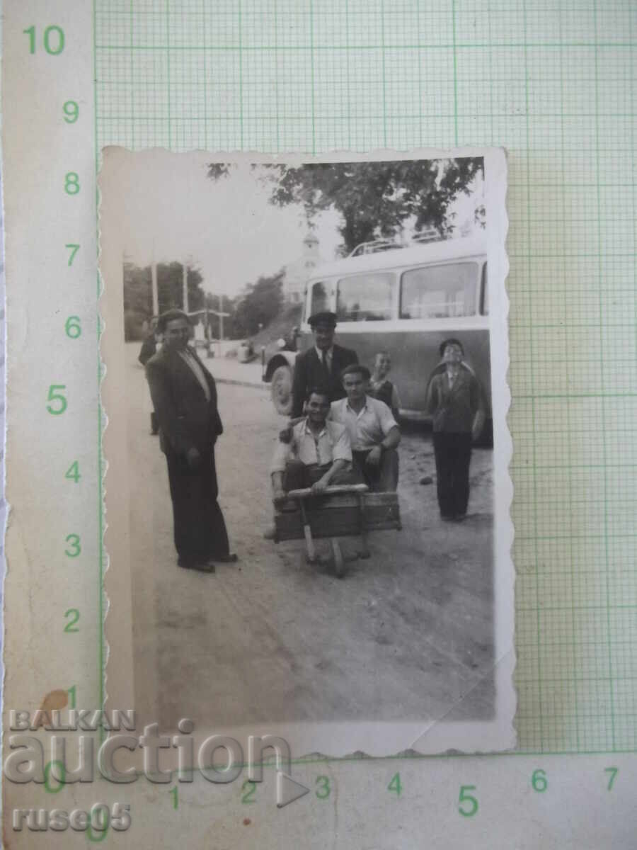 Φωτογραφία δύο ανδρών σε ξύλινο καρότσι δίπλα σε παλιό λεωφορείο