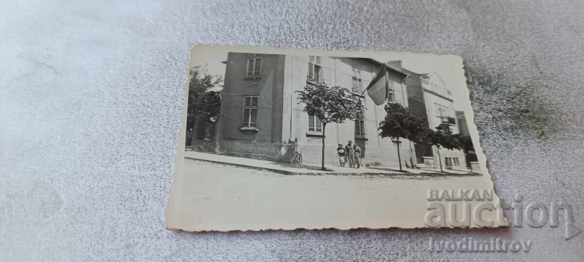 Photograph of a man and two women in front of a two-story house