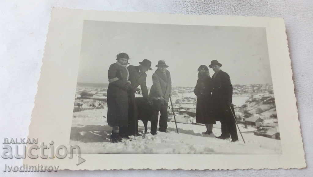 Φωτογραφία Γυναίκες και άνδρες με ένα μαύρο κριό πάνω από το χωριό το χειμώνα