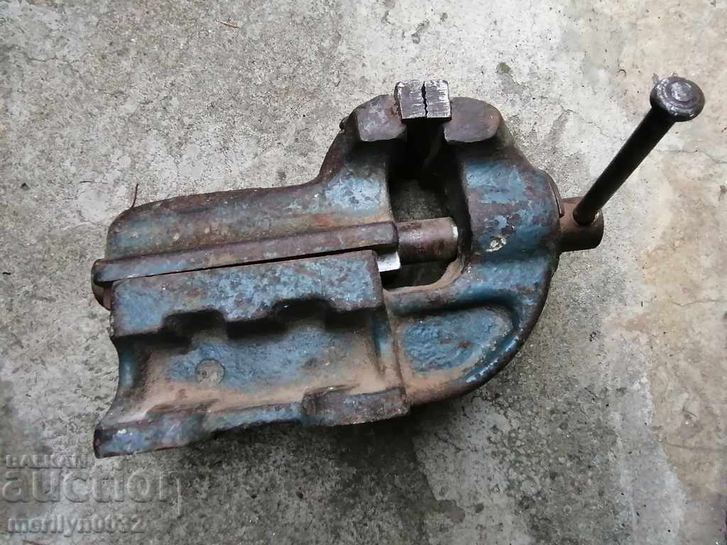 An old vise clamps an iron tool from the SOC WORKS