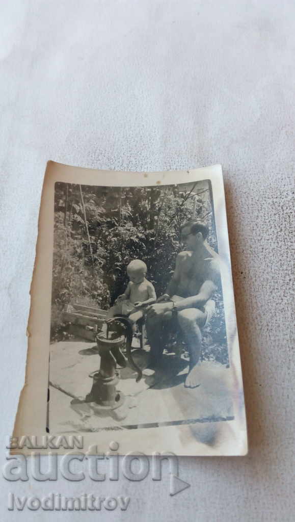 Photo Man in shorts with his son next to a water pump
