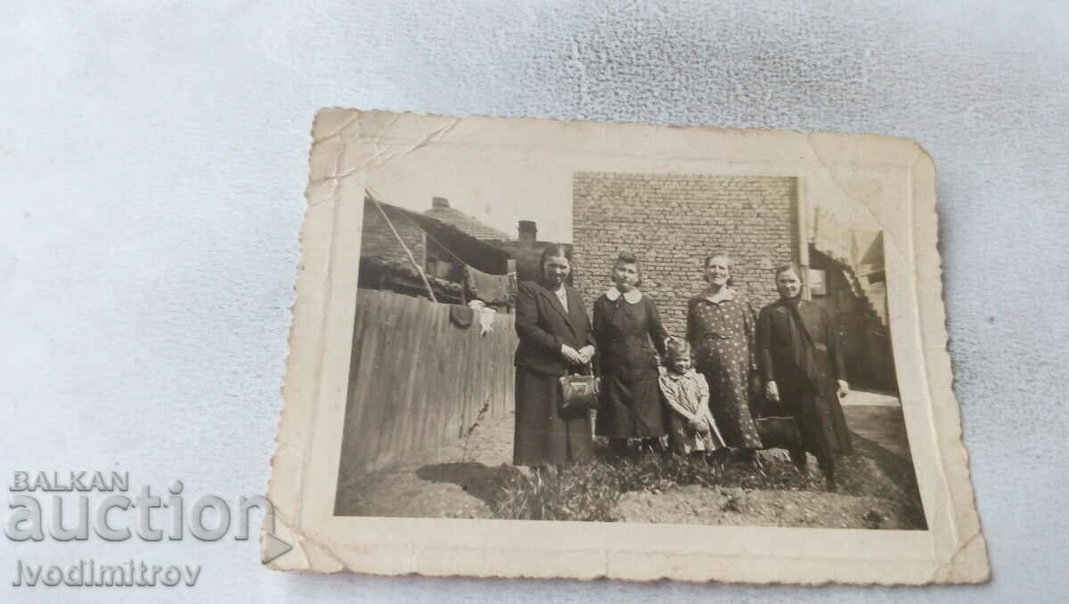Φωτογραφία Τέσσερις γυναίκες και ένα κορίτσι κοντά στο φράχτη ενός σπιτιού