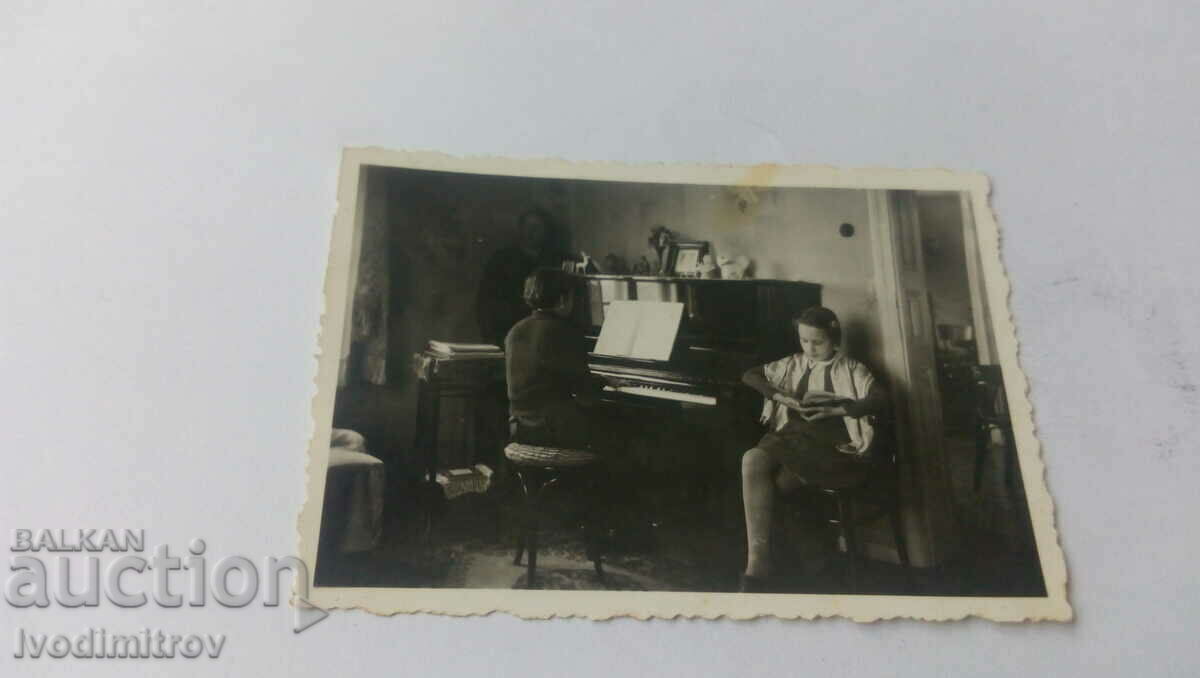Photo A boy is playing the piano and a girl is reading a book