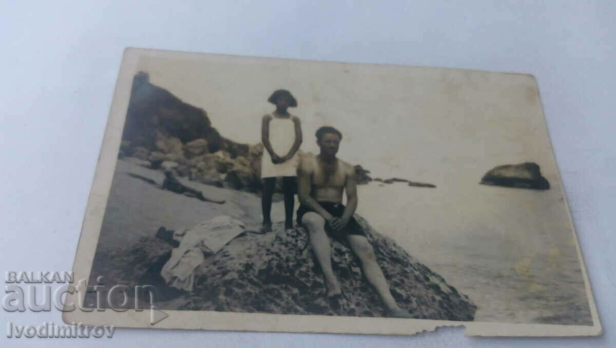 Fotografie cu un bărbat și o fetiță pe o stâncă lângă mare