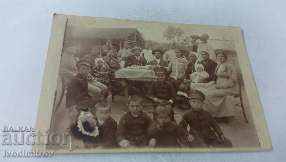 Picture Men, women and children at a table in the yard of their house