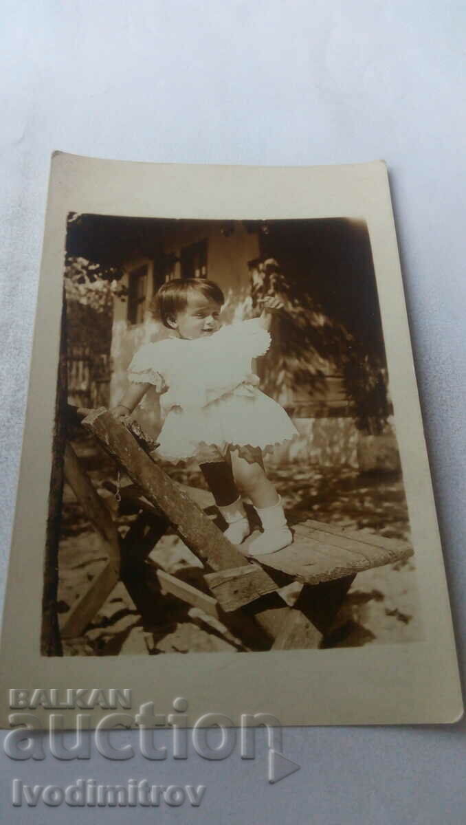 Снимка Малко момиченце облечено в бяло на стол в двора