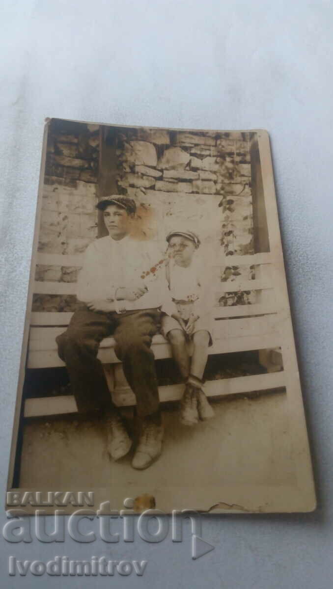Photo A man and a boy on a wooden bench next to their house
