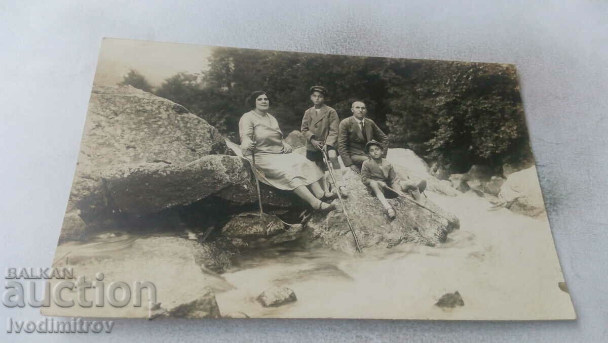 Photo Man, woman and two boys on stones by a stream