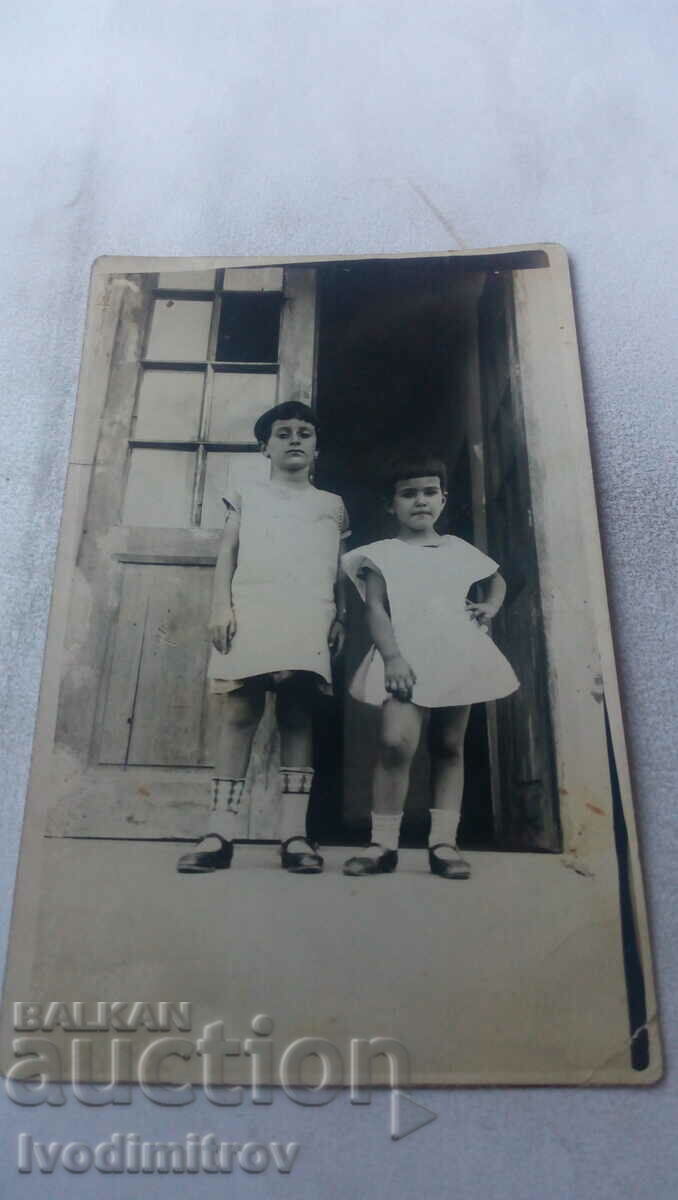 Foto Două fetițe în fața intrării unei case