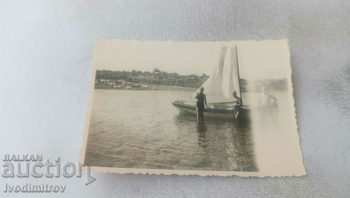 Photo Three men in front of a sailboat in the sea