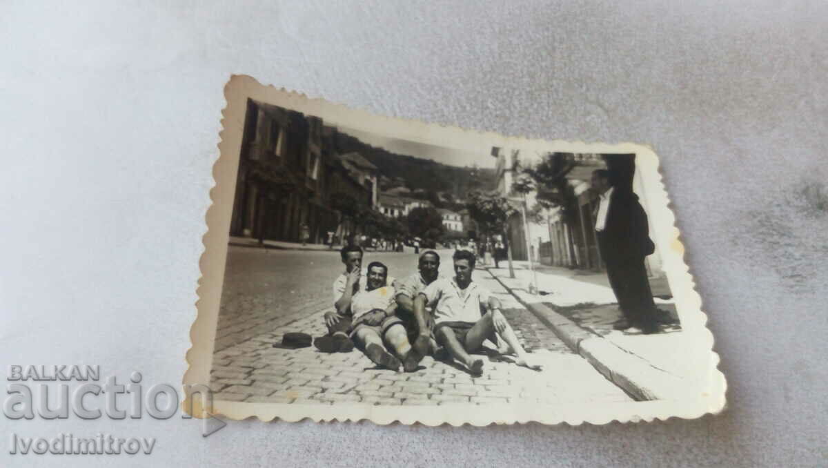Φωτογραφία Τέσσερις νεαροί άνδρες που κάθονται σε έναν πλακόστρωτο δρόμο