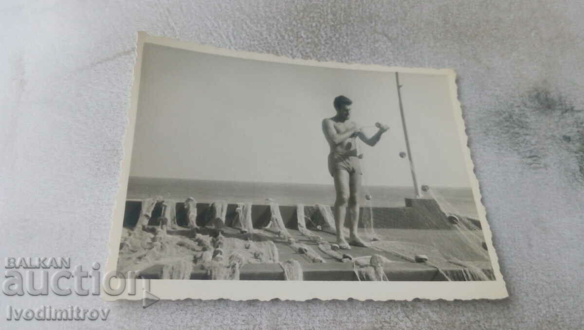Снимка Мъж по бански оправя риболовна мрежа на кораб
