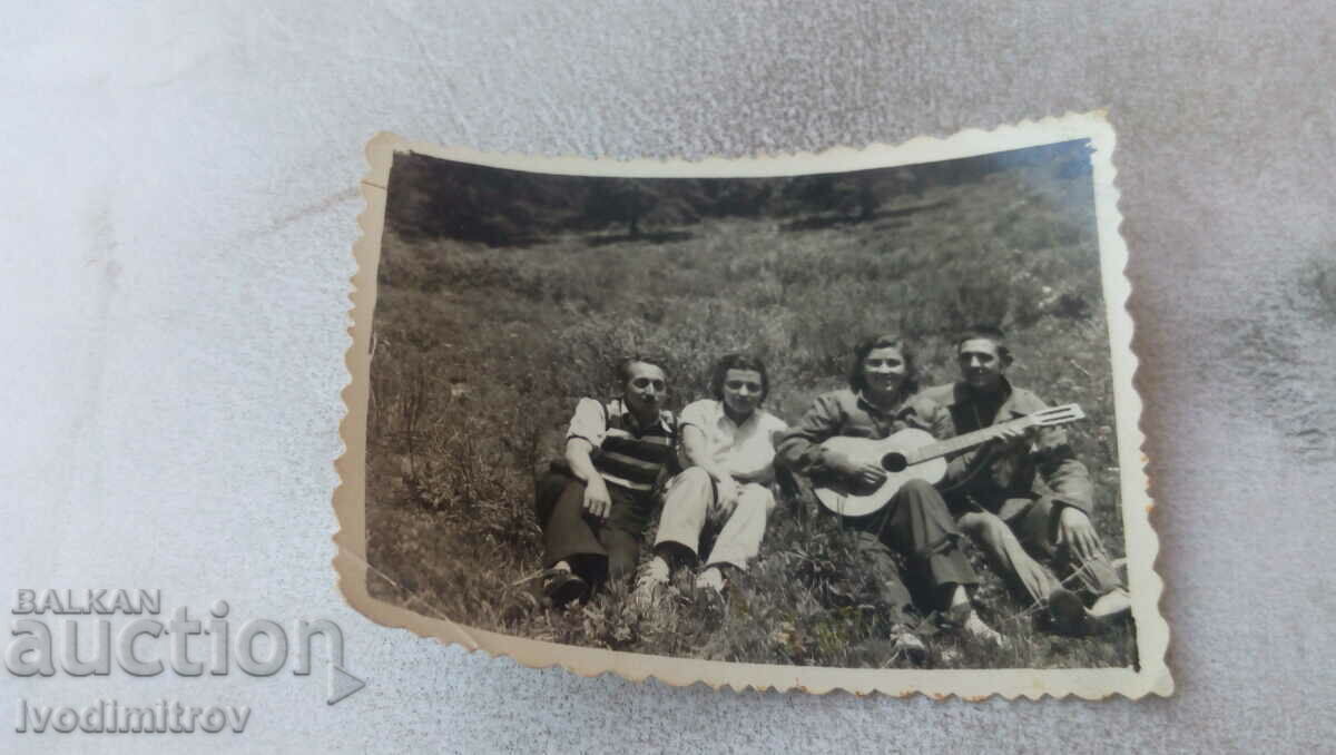Photo Two young men and two girls with a guitar on the grass