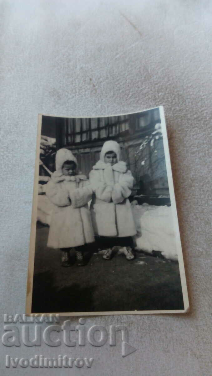 Снимка Две малки момичета с бели зимни палта на улицата