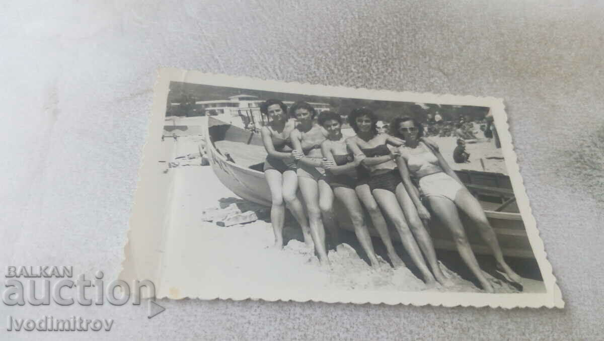 Foto Cinci femei în costume de baie de epocă lângă o barcă pe plajă