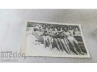 Photo Five women in vintage swimsuits next to a boat on the beach