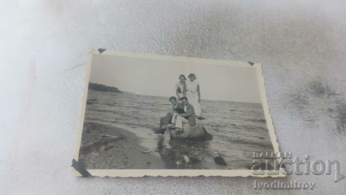 Φωτογραφία Δύο άντρες και δύο κορίτσια σε μια πέτρα στην παραλία