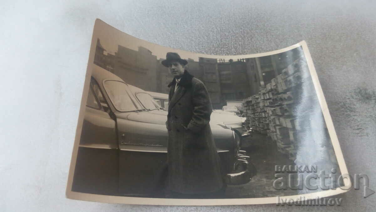 Photo A man in a winter coat next to an Olympia car