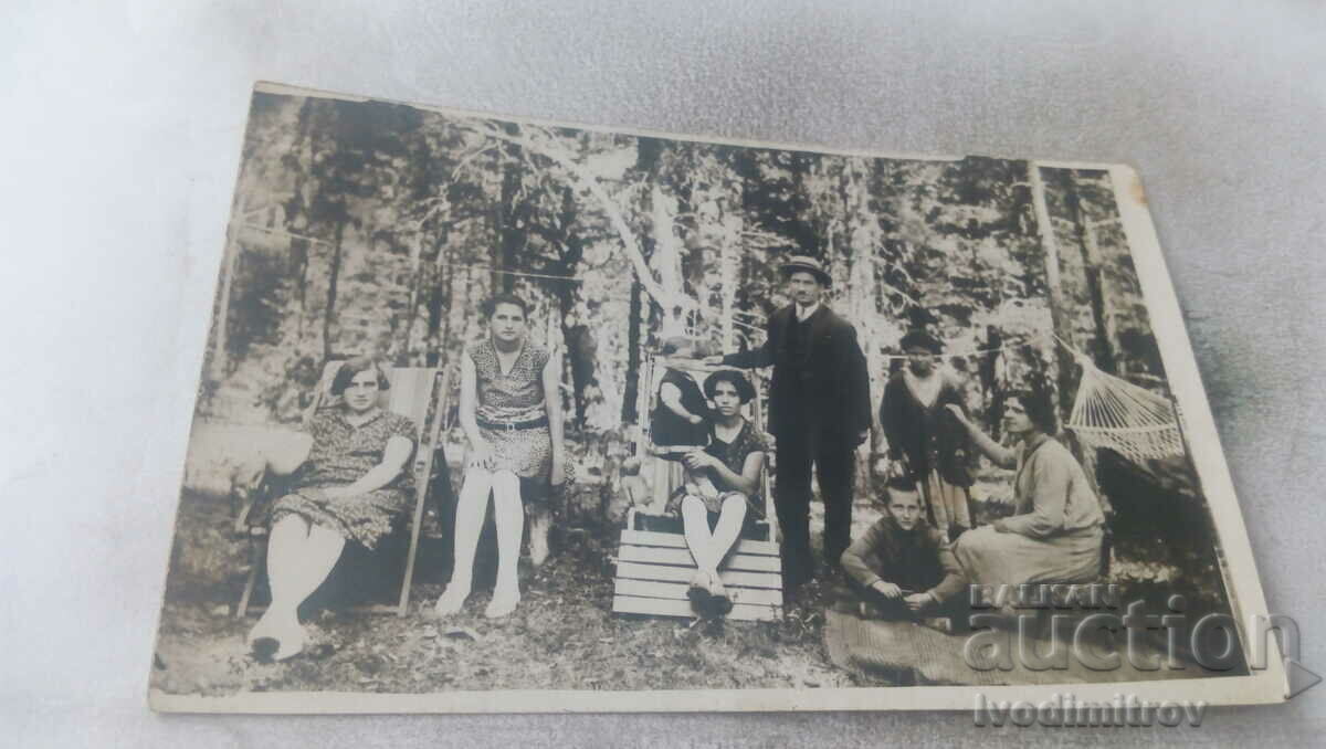 Fotografie Bărbați, femei și copii pe șezlonguri din lemn în pădure