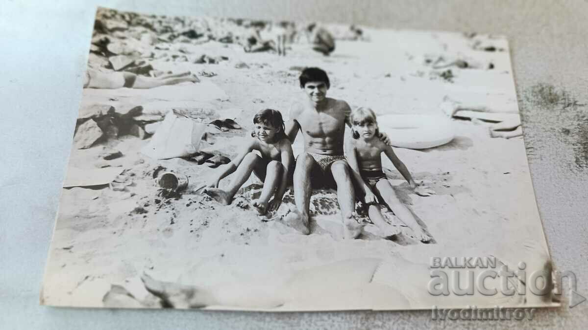 Photo A young man and two little girls on the beach