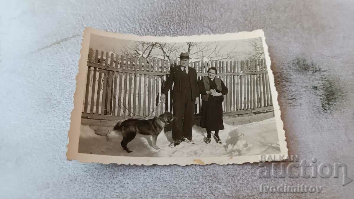 Fotografie Bărbat femeie și câine în fața unui gard de lemn iarna