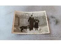 Fotografie Bărbat femeie și câine în fața unui gard de lemn iarna