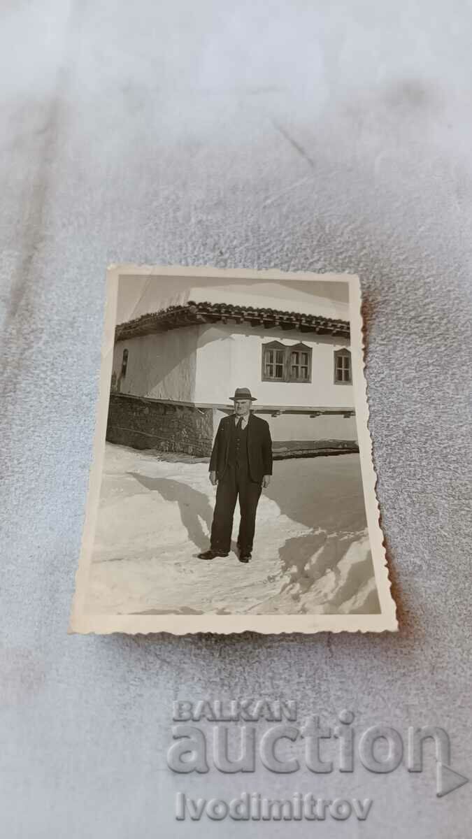 Photo A man in a suit in front of an old country house in winter