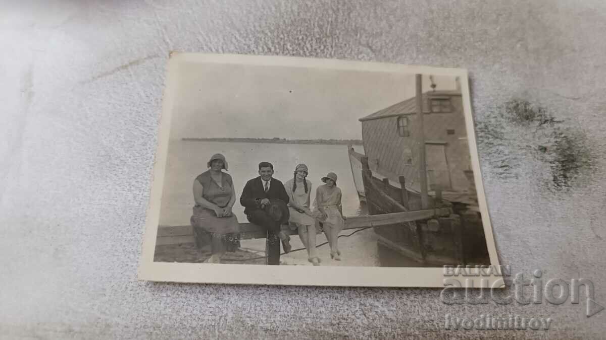 Photo A man and three women sitting on a board at the harbor